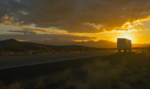 Sunset View of Semi Truck Driving Away from Camera